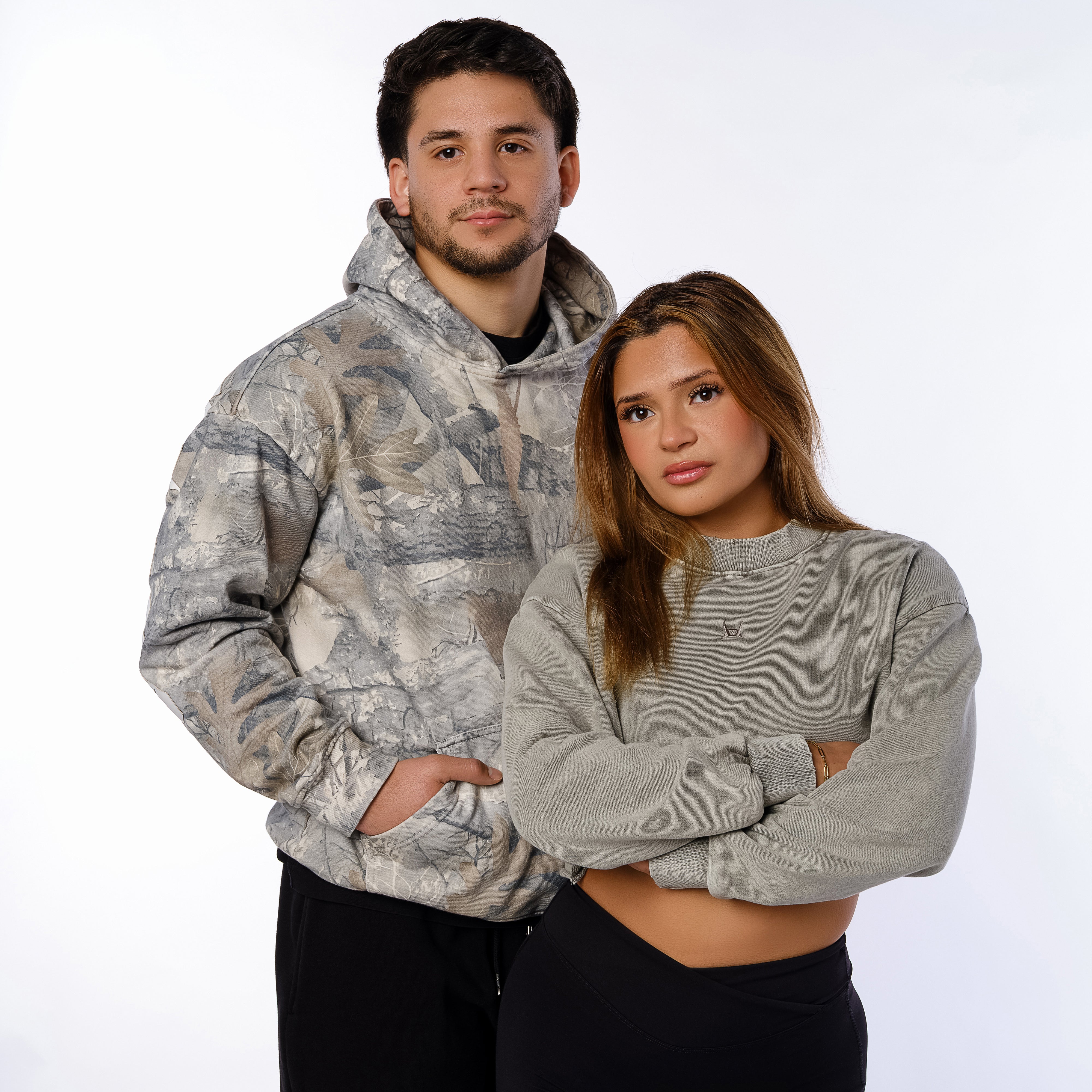 Two people wearing gray hoodies standing against a white background