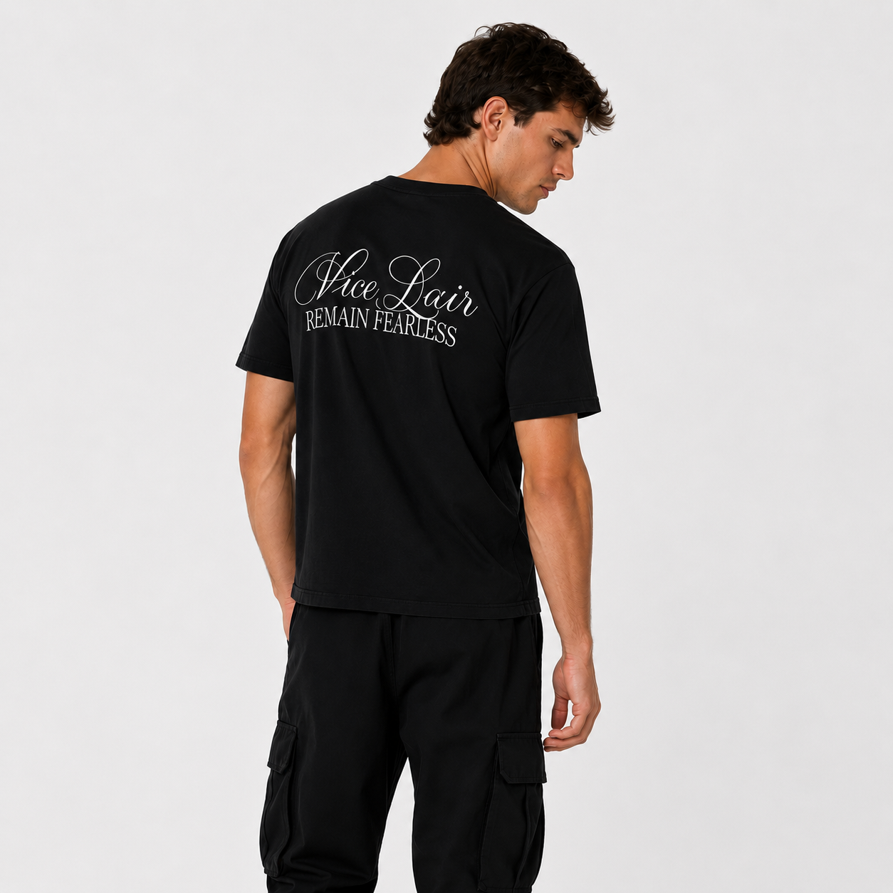 A man wearing a black t-shirt with 'Vice Lair Remain FEARLESS' printed in white script on the back, shown from a rear three-quarter view against a light gray studio background.