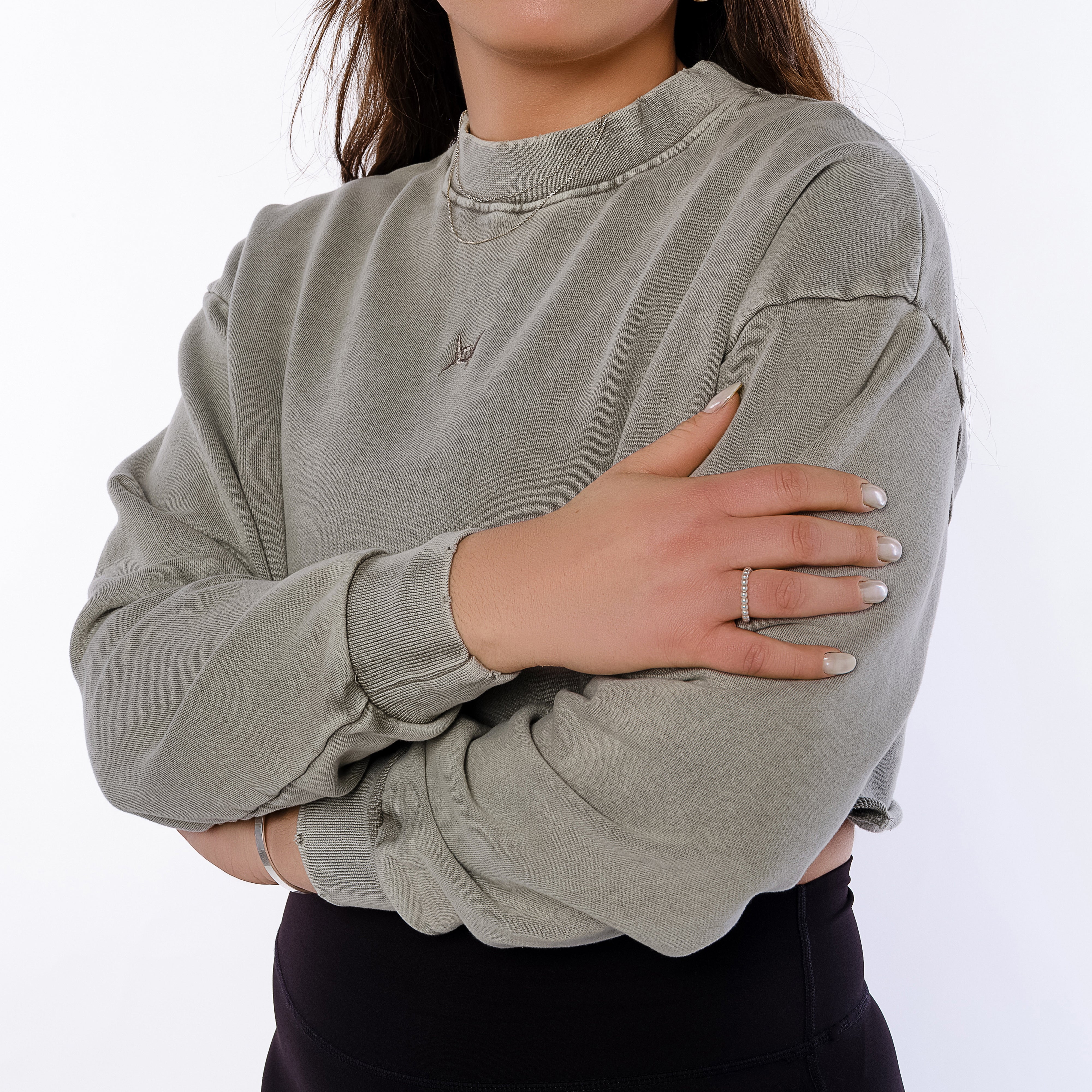 Person wearing a gray sweatshirt with arms crossed on a white background